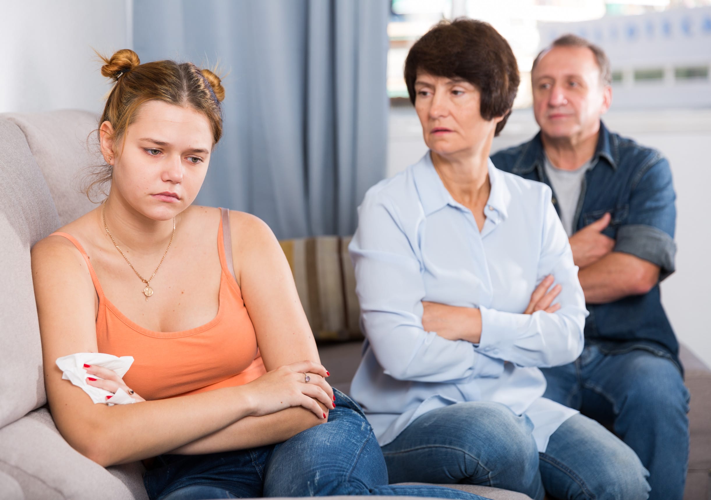 Mom and dad are supporting a sad daughter on sofa at home.