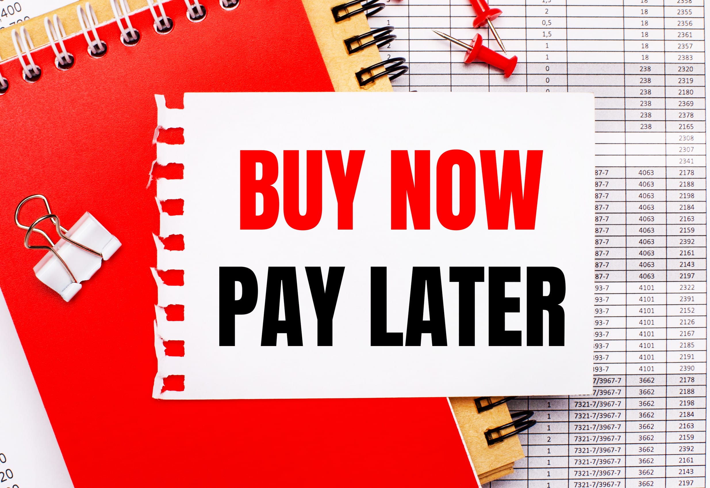 Against the background of the reports, there are red and brown notepads, a white paper clip, red buttons and a white sheet of paper with the text BUY NOW PAY LATER. Business concept