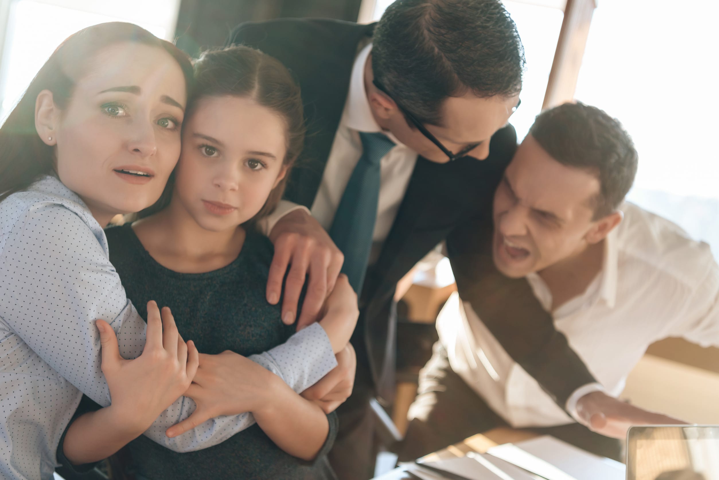 Family lawyer is holding back invasive adult man who is trying to hit restless wife with daughter. Dissolution of marriage of two adults. Two parents fighting over child in divorce concept.