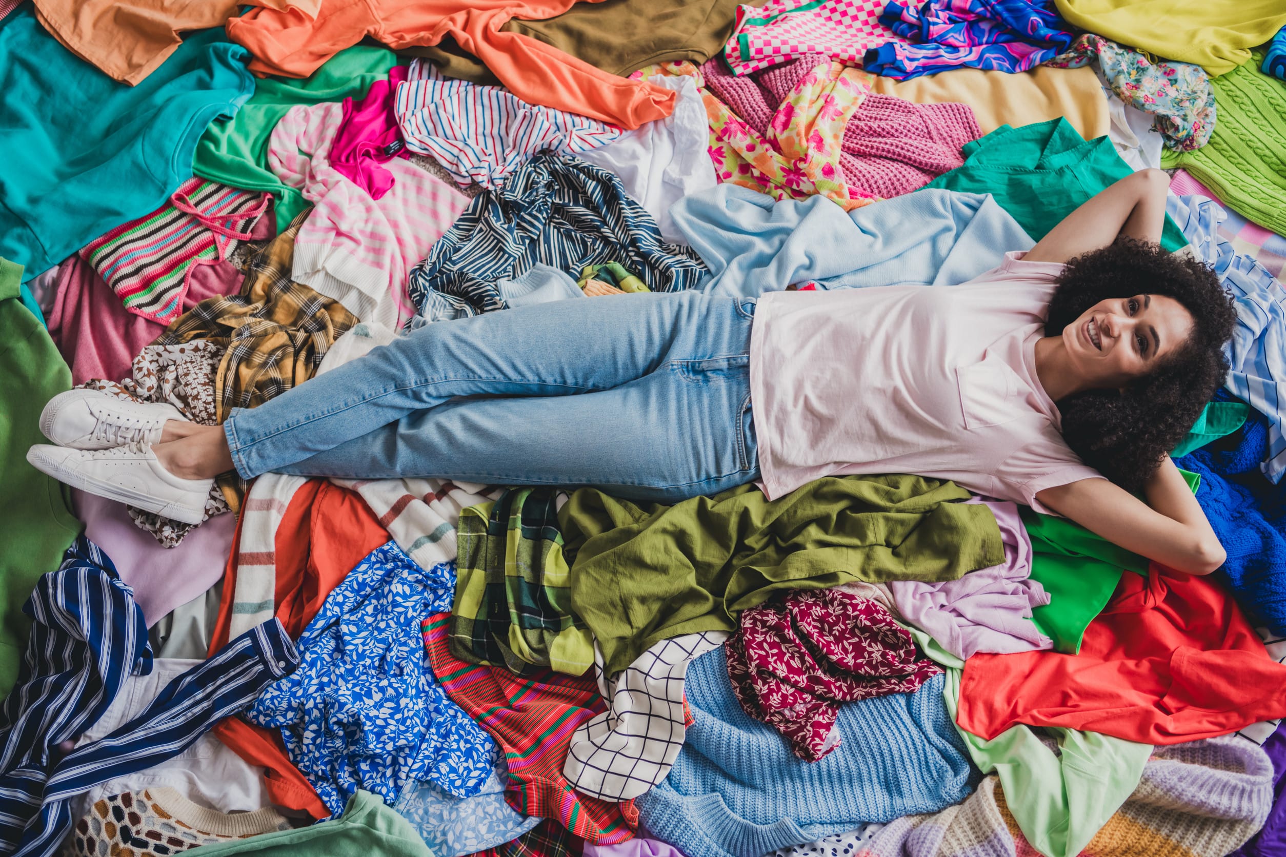 Full size above view photo of young woman laying messy pile stack clothes apartment indoors.