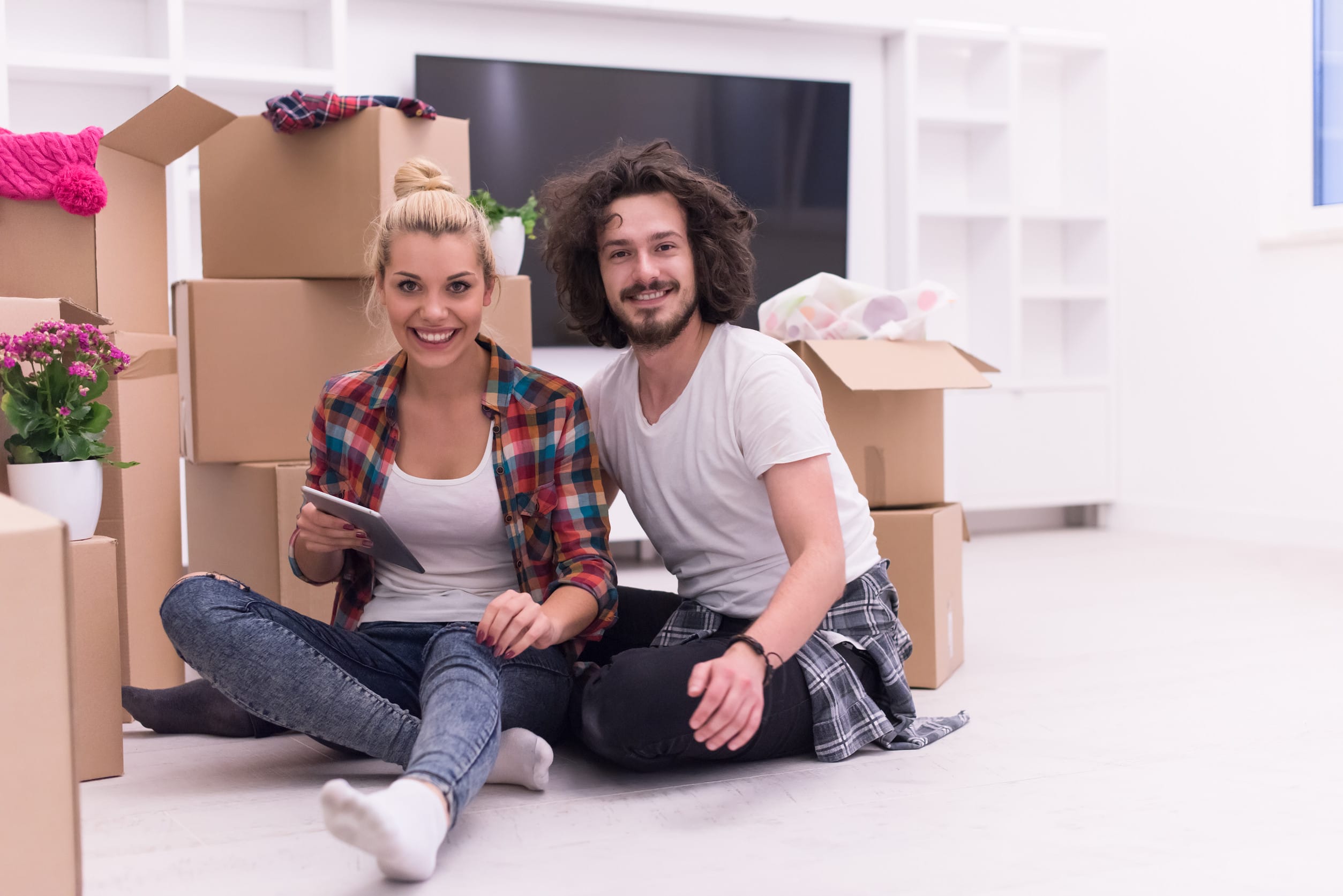 Relaxing in new house. Cheerful young couple sitting on the floor while cardboard boxes laying all around them
