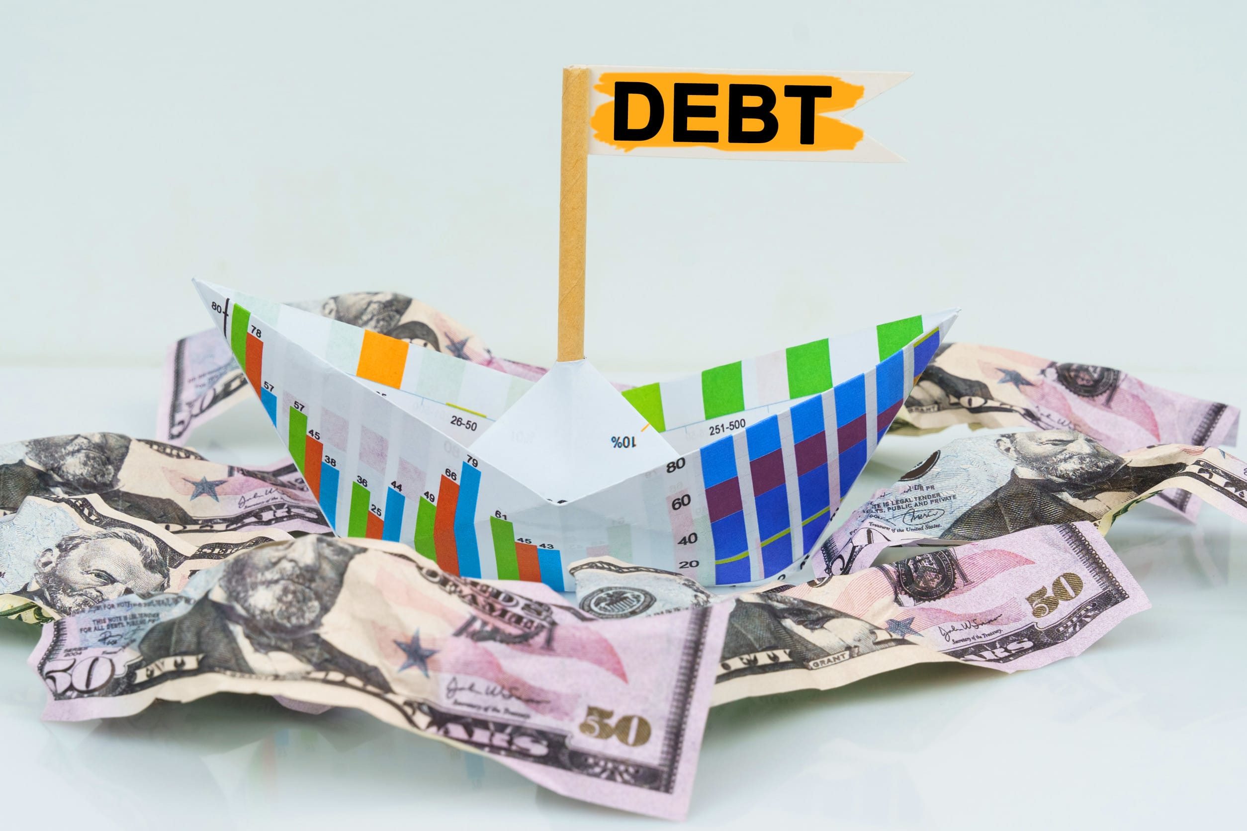 Business and finance concept. A paper boat from a business graph floats on a sea of money. The text is written on the flag - DEBT