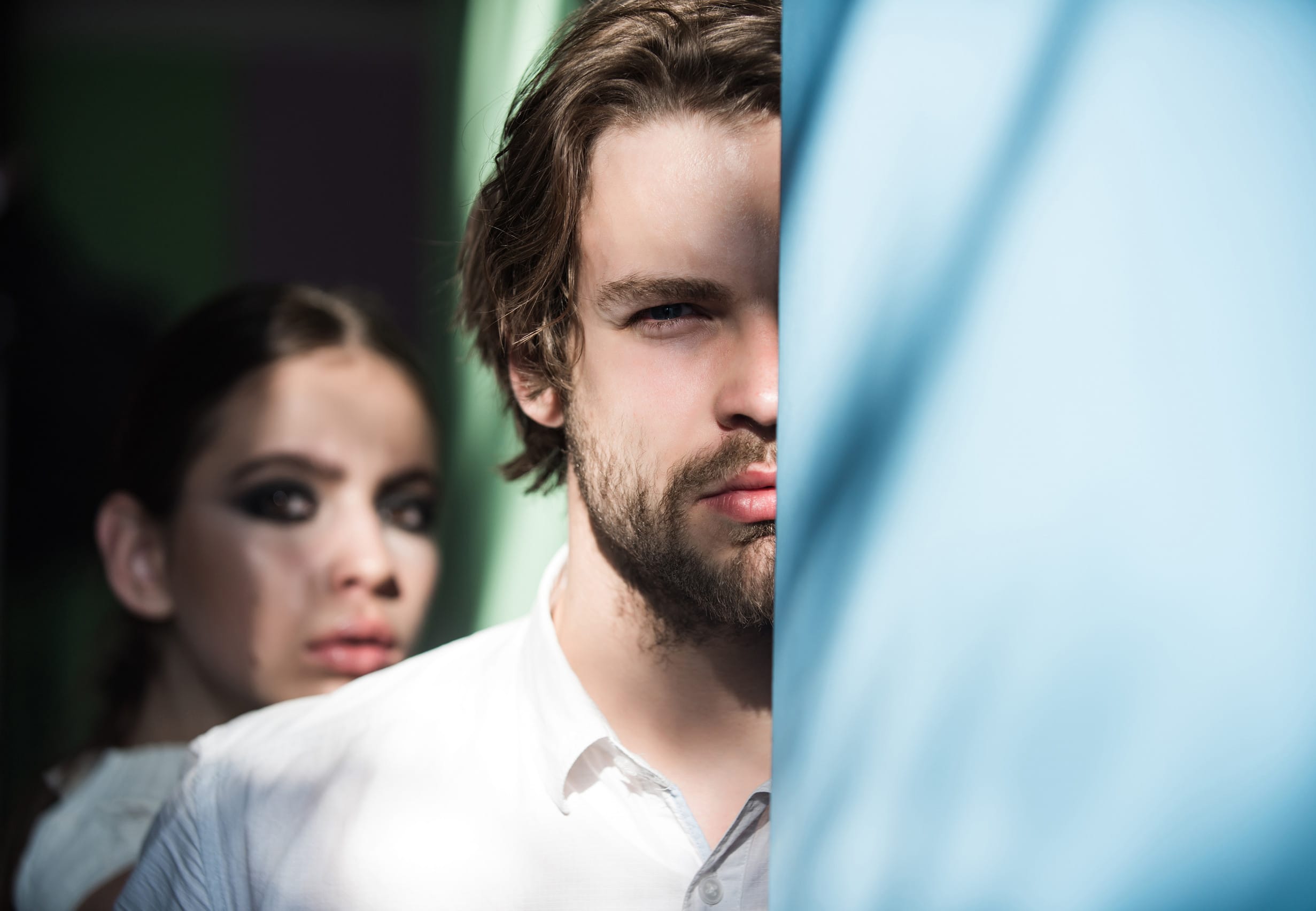 Macho hide half face with beard at blue wall and blurred girl on background. Fashion, beauty, relationship concept, copy space
