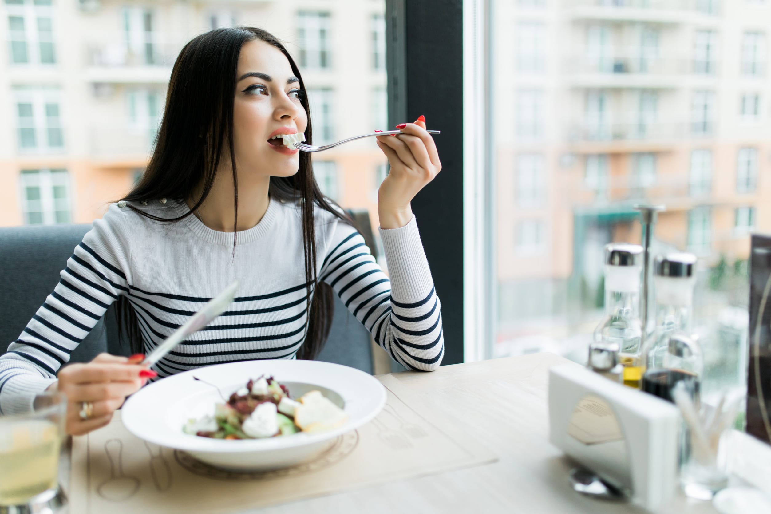 Young woman eating healthy food sitting in the beautiful interior with green flowers on the background