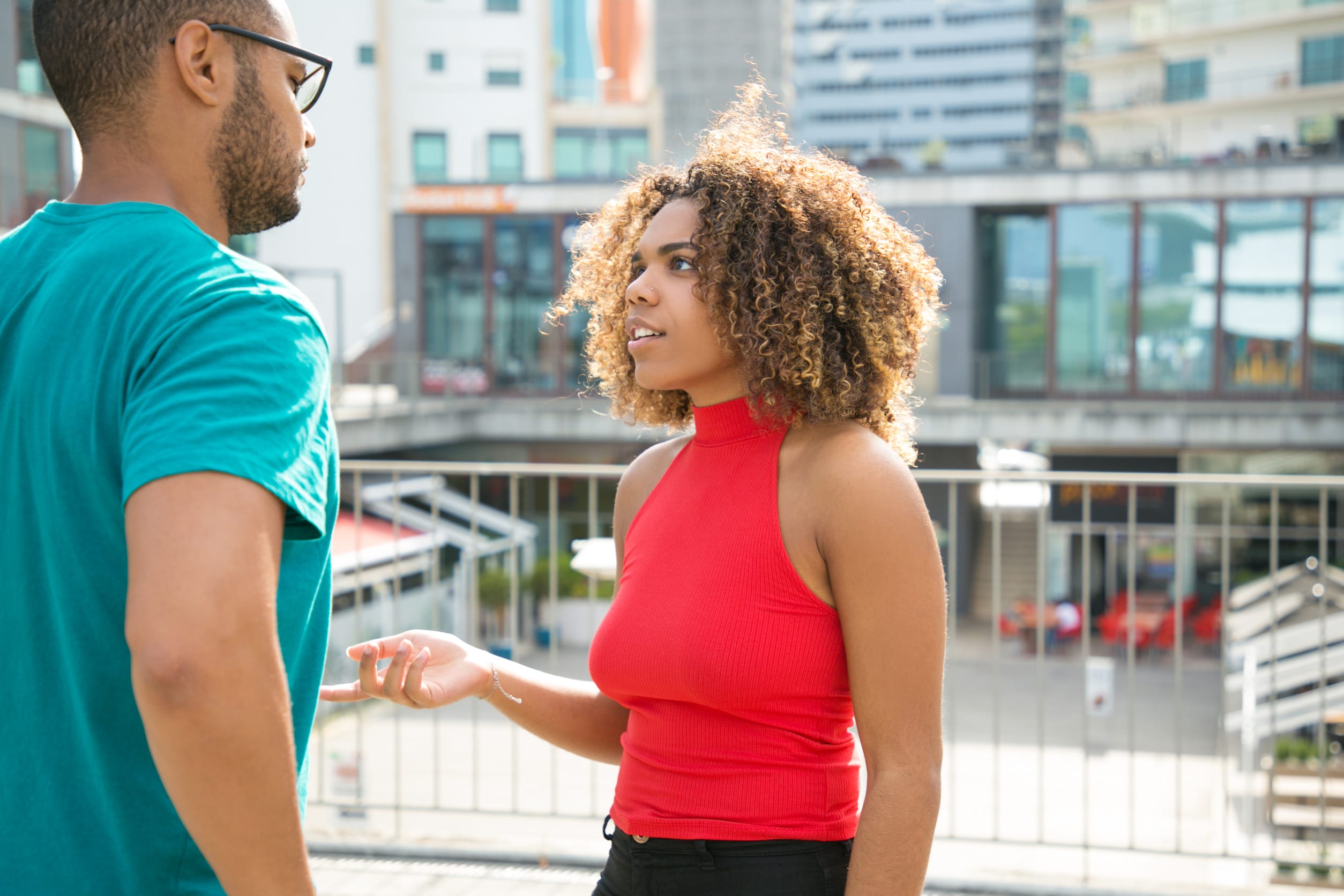 Shocked black girl getting surprising news from her male friend. Mix raced friends standing on outdoor building terrace and talking. Couple of friends concept