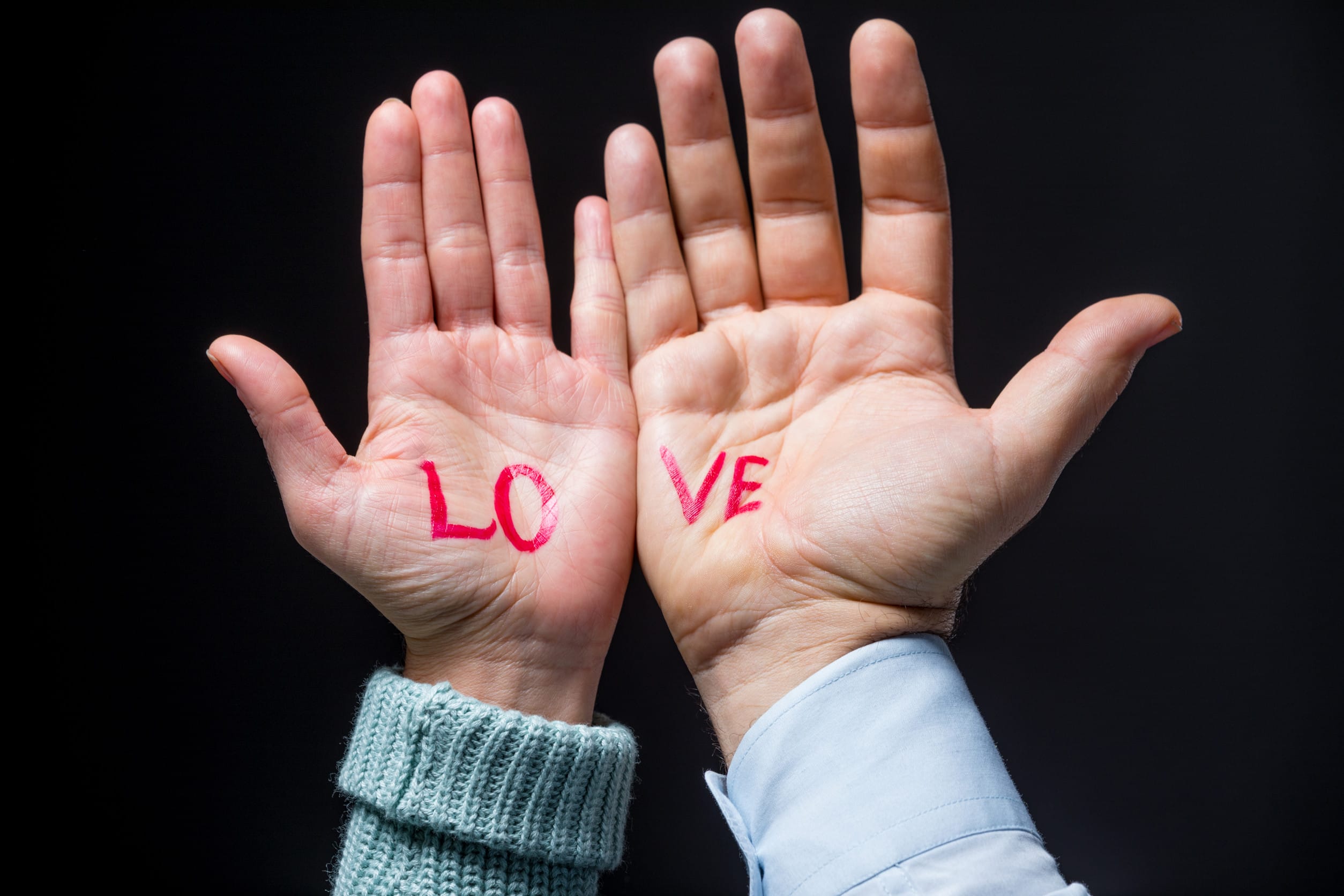 Close-up view of male and female hands with word love on black