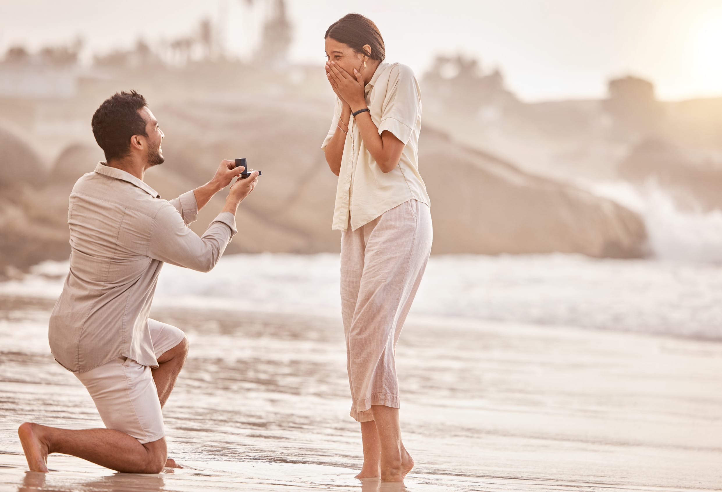 a young man proposing to his girlfriend on the beach.