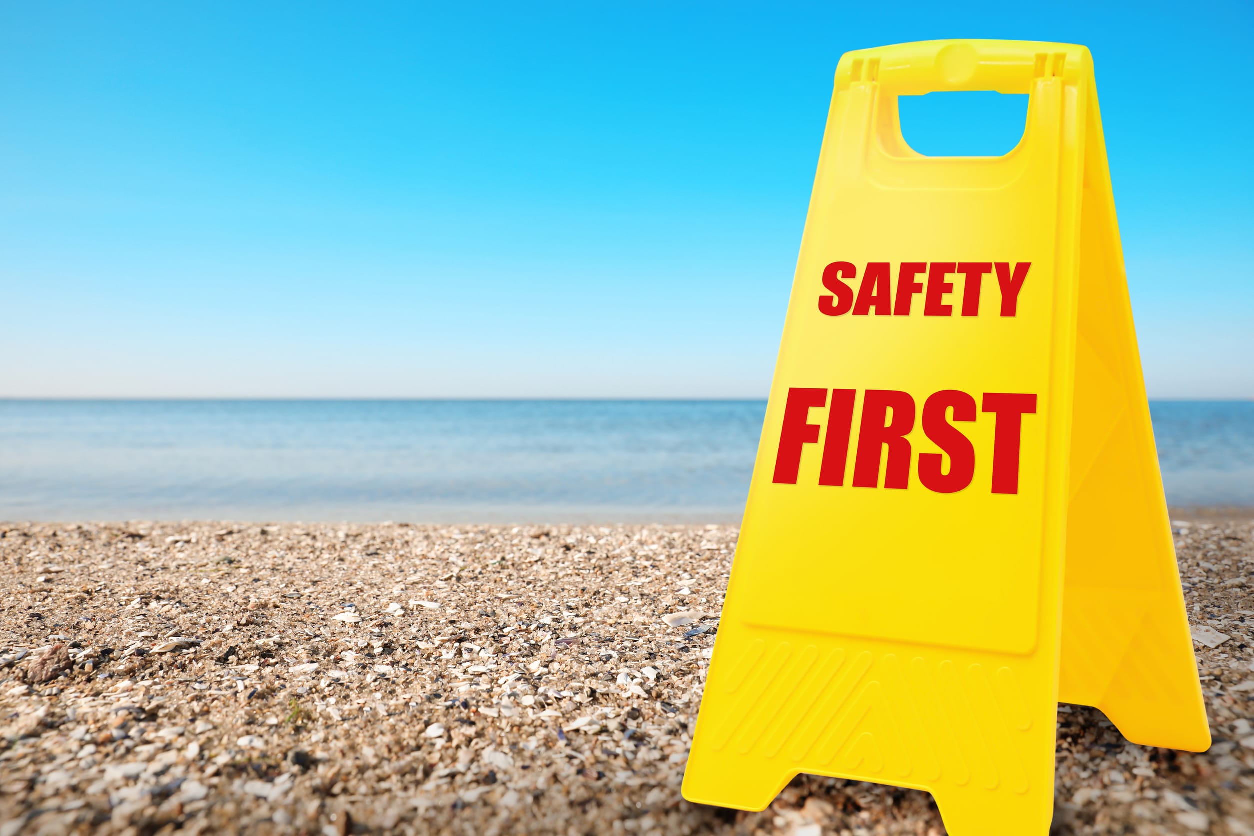 Sign with phrase SAFETY FIRST on sandy beach, space for text