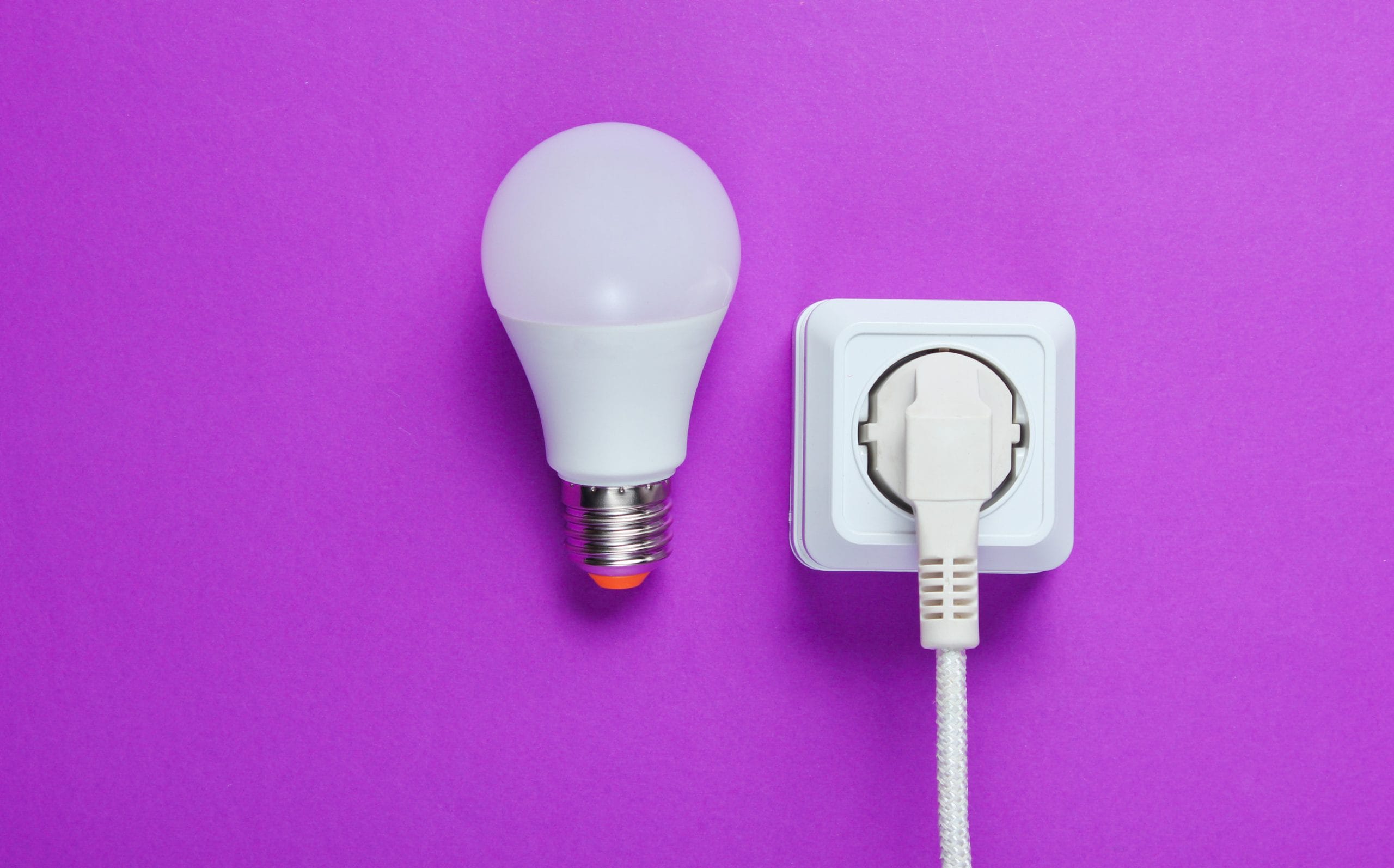 White cable plugged into power outlet and LED light bulb on purple background. Top view