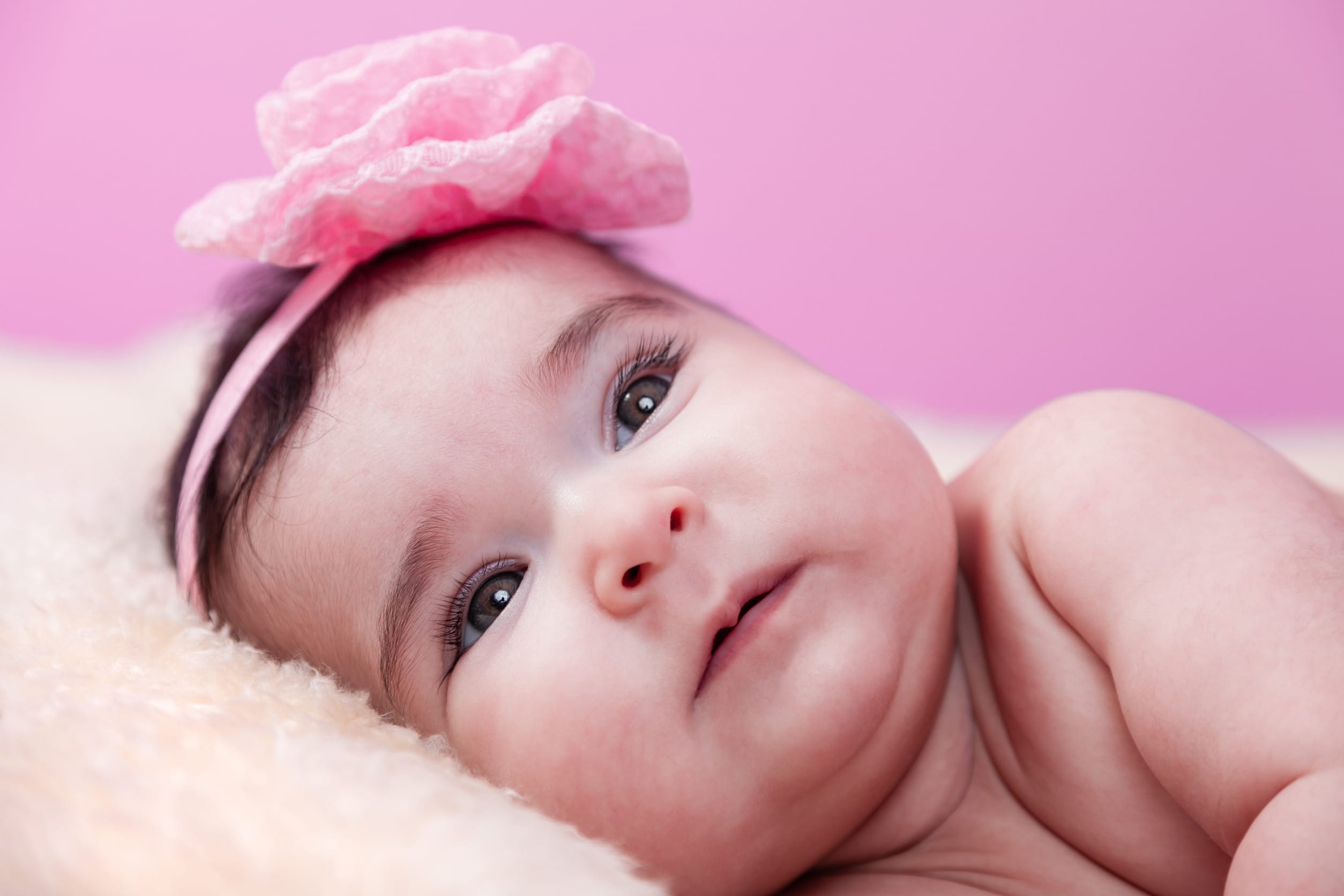 Cute, pretty, happy, chubby baby girl portrait smiling. Lying naked or nude on fluffy blanket. Pink flower headband. Four months old