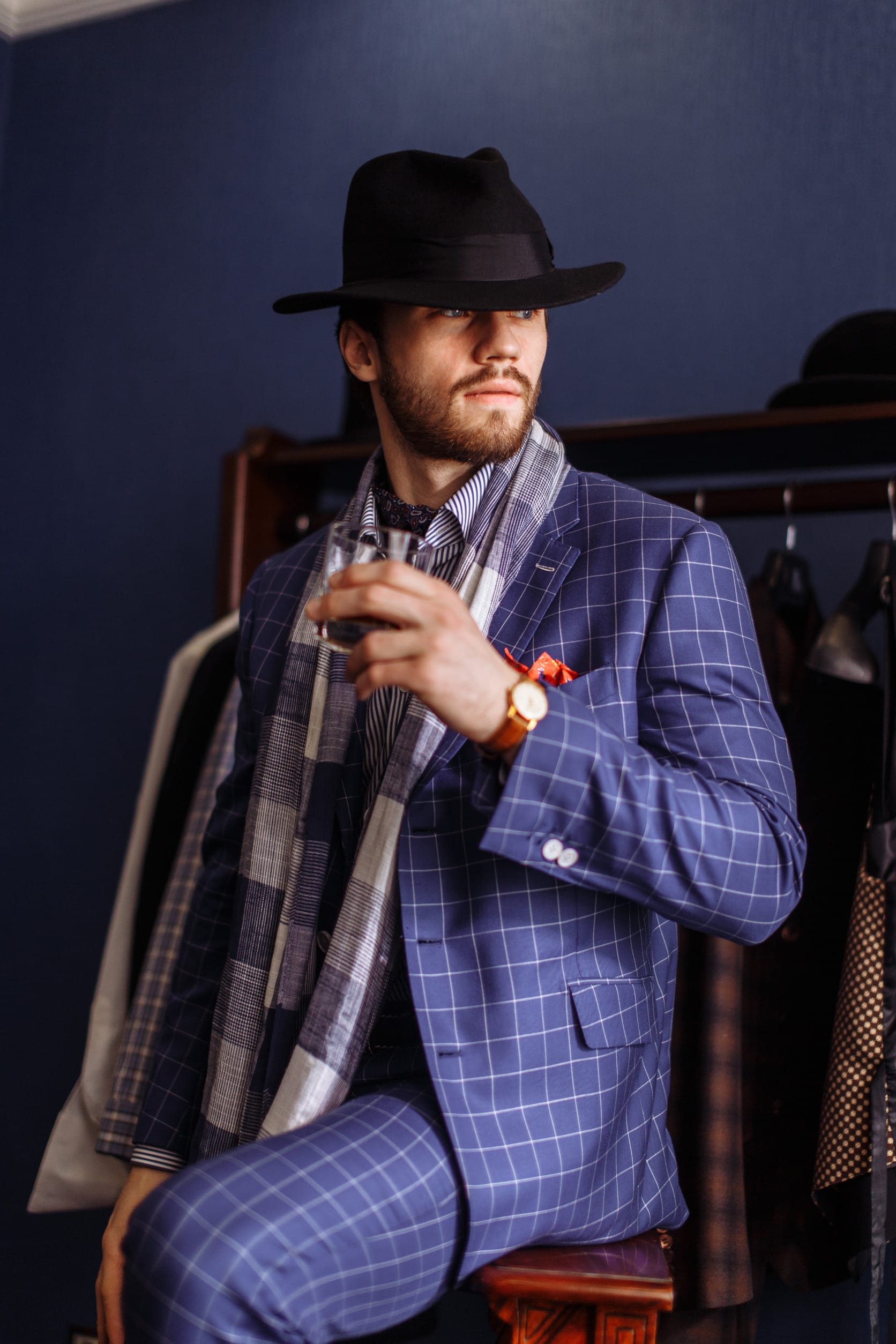 Elegant young businessman in classic suit and hat sitting at atelier with beverage