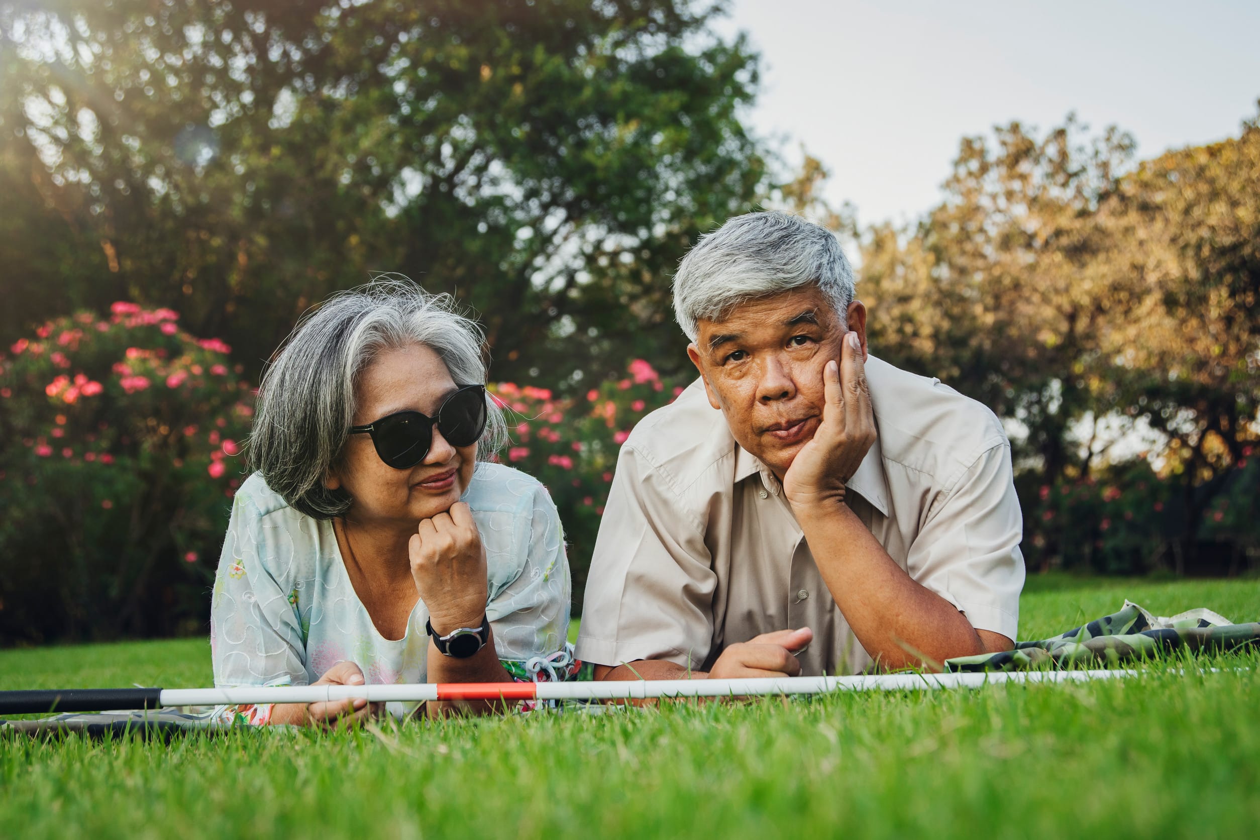 Portrait elderly couple whose blind wife sleeps on the lawn with her husband posing for a photo together. Their hearts are bright because they have a loving and caring husband always by their side.