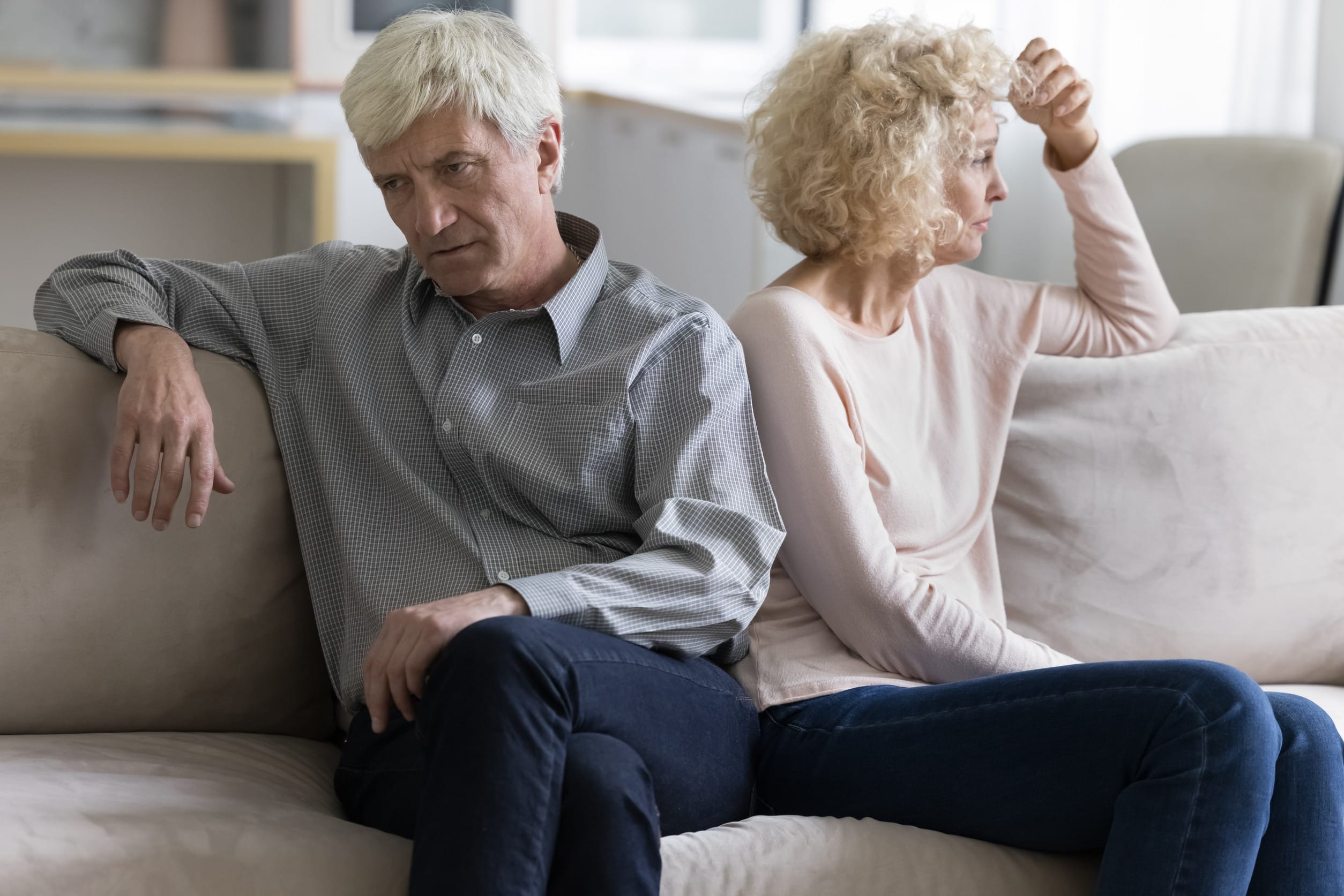 Offended annoyed upset mature older couple tired of each other, sitting on home sofa in silence, looking away, thinking over relationship problems, divorce, breakup, family crisis