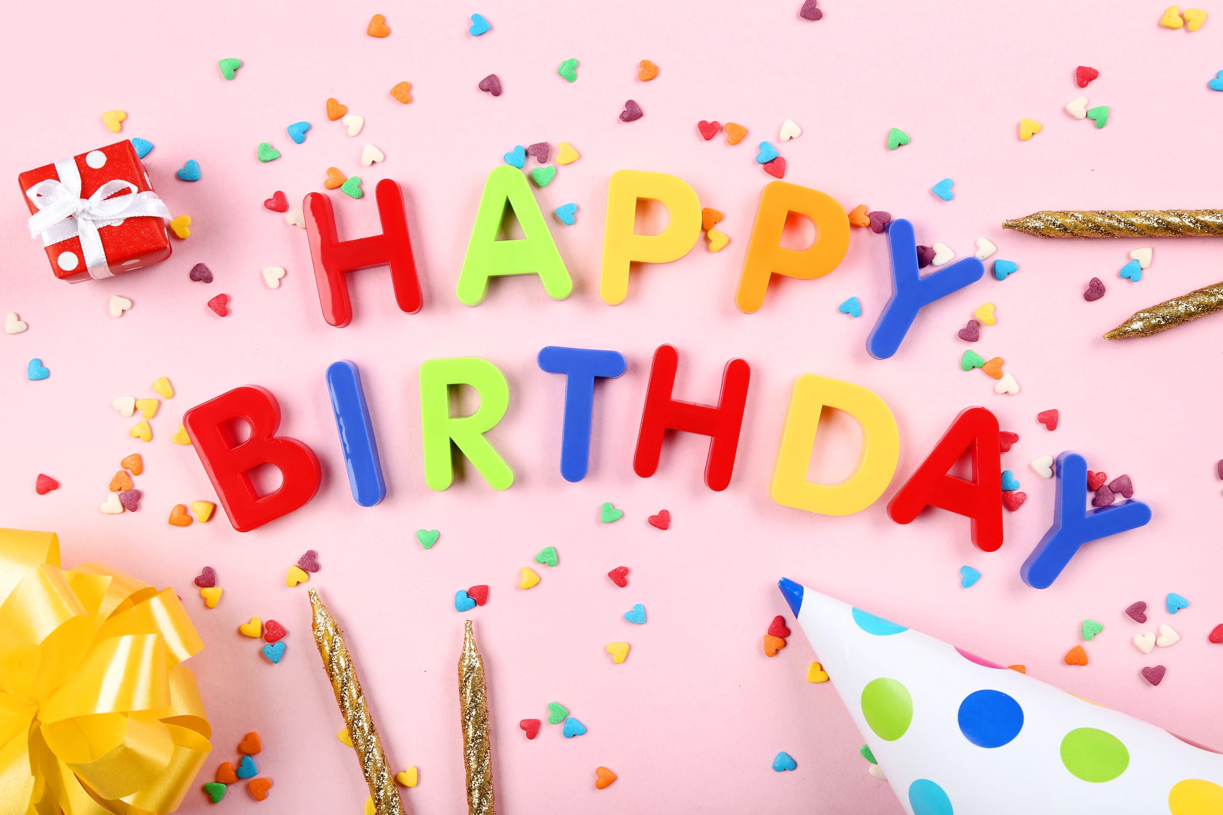Text Happy Birthday by plastic letters with candles and sprinkles on pink background