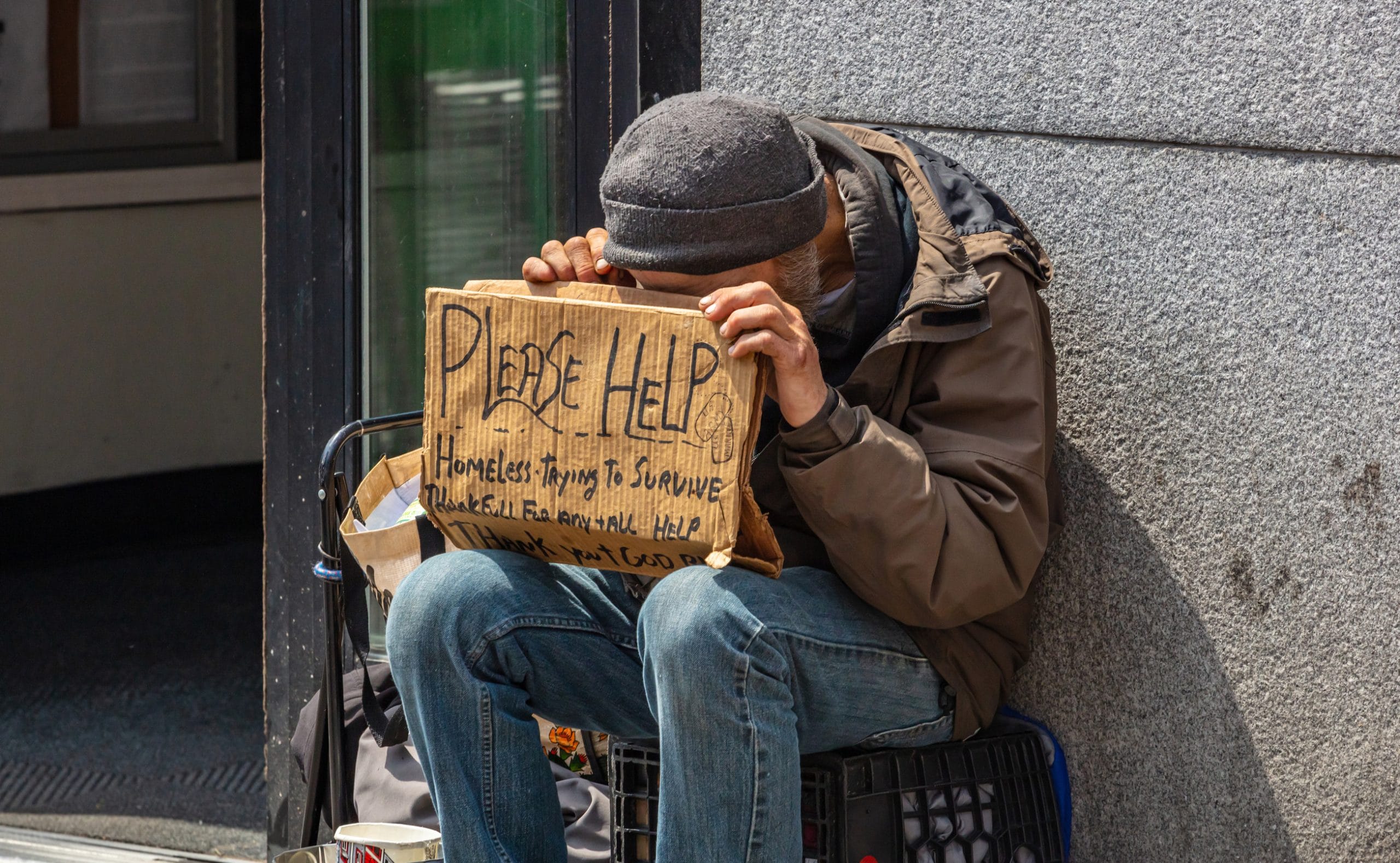 Homeless man holding a cardboard sign, asking for help, Manhattan downtown, sunny day in spring