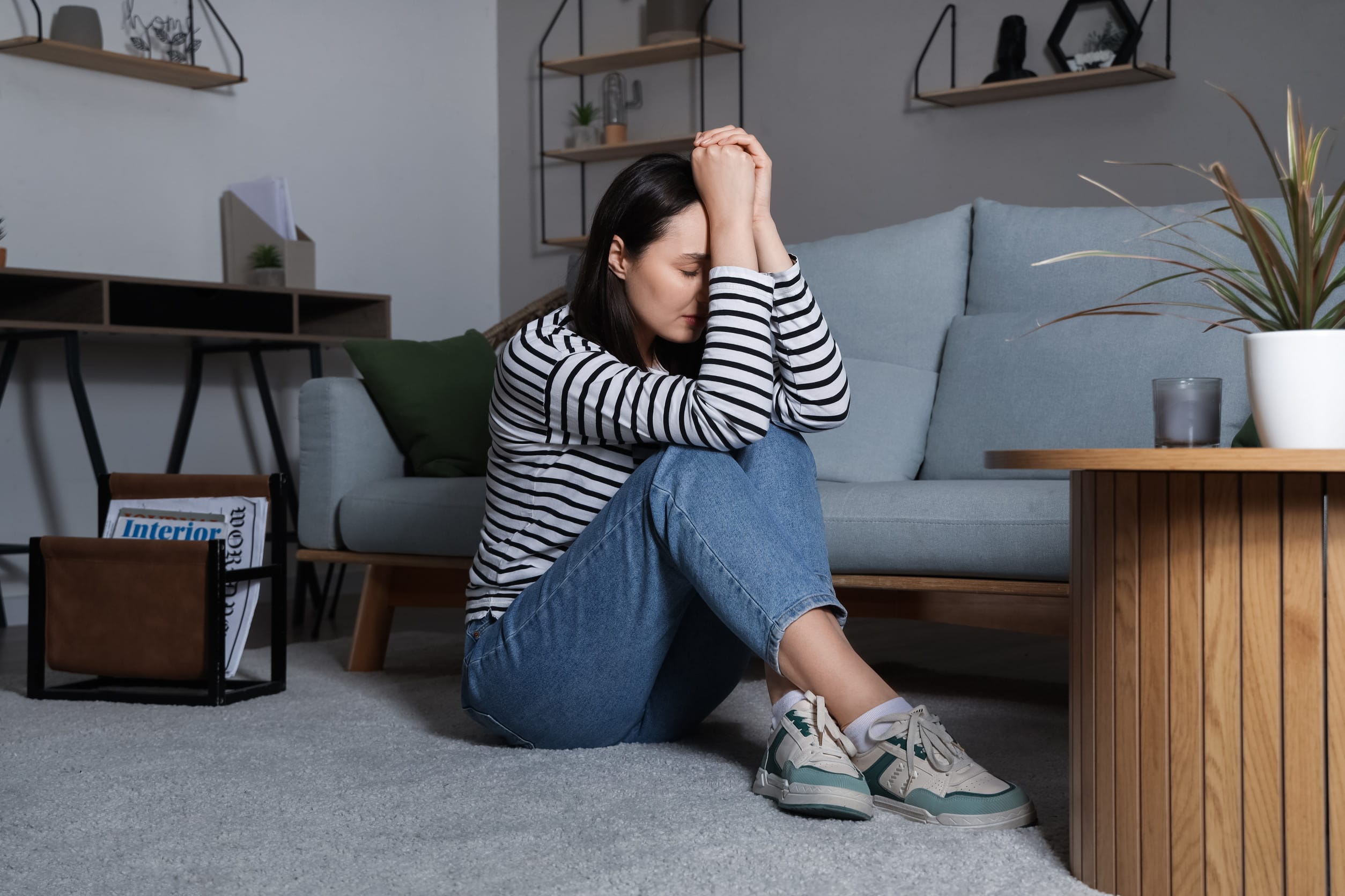 Depressed young woman sitting on floor at home