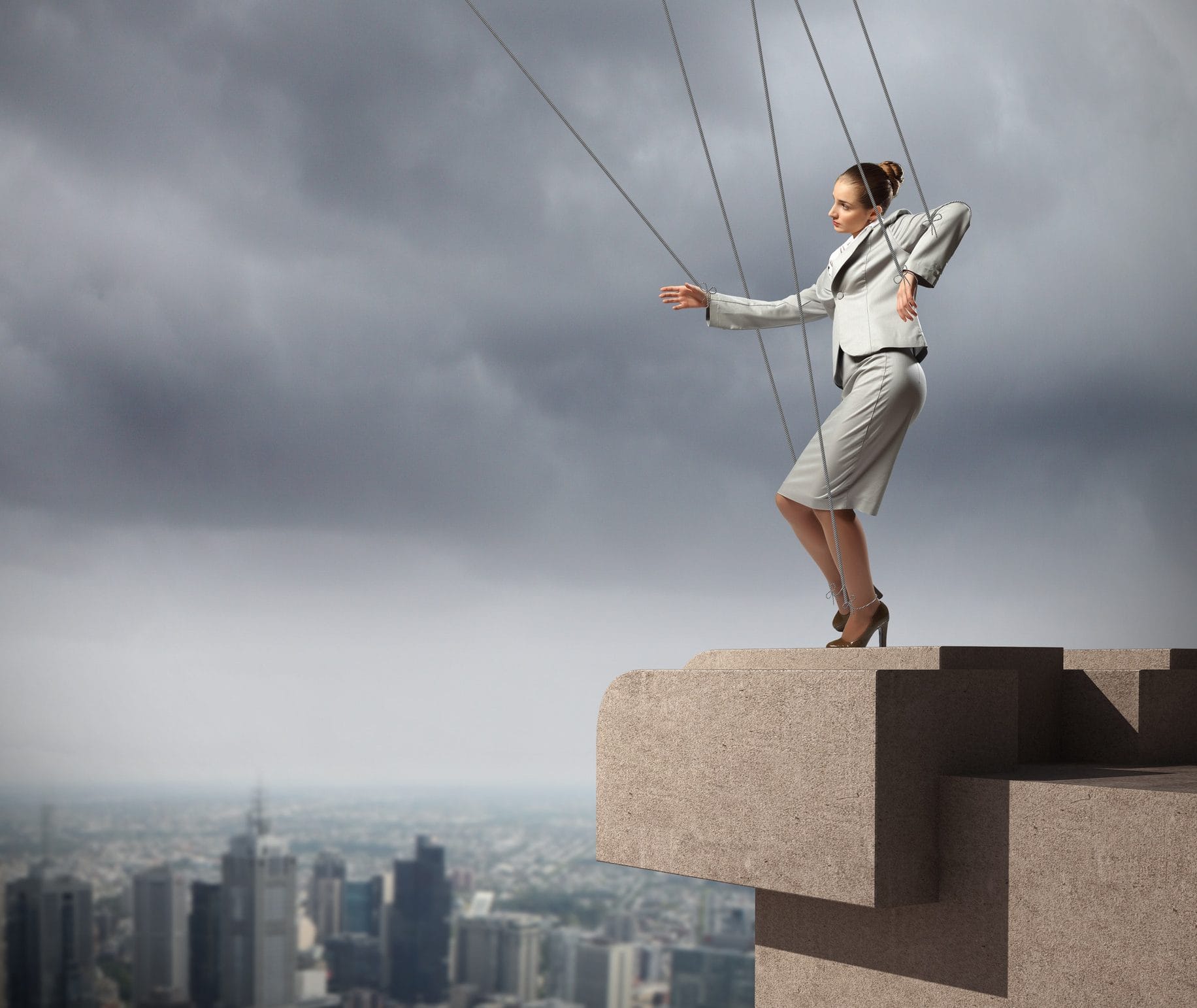 Businesswoman marionette on ropes controlled by puppeteer against city background