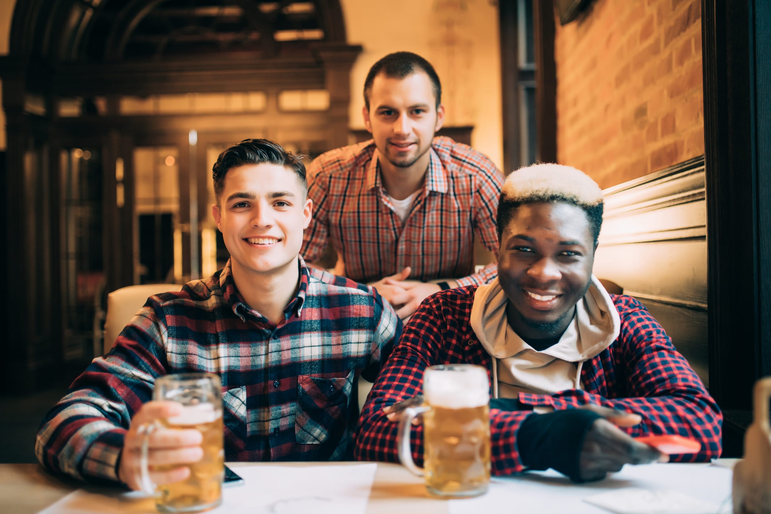 Multiracial friends group drinking and toasting beer at pub. Young people enjoying time together and having fun.