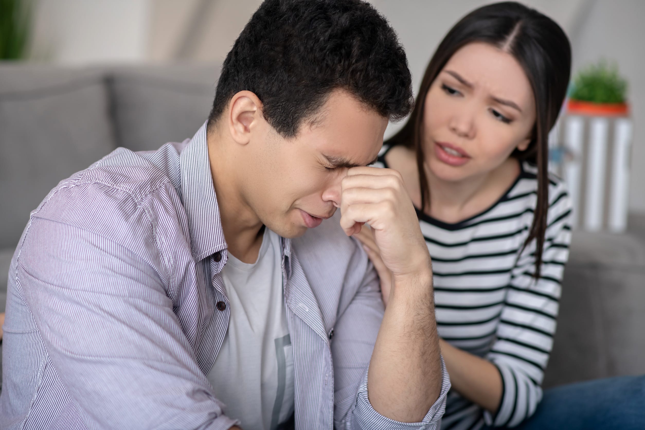 Difficult situation. Young man with eyes closed hand near the eyes, and a sympathetic woman carefully looking and talking.