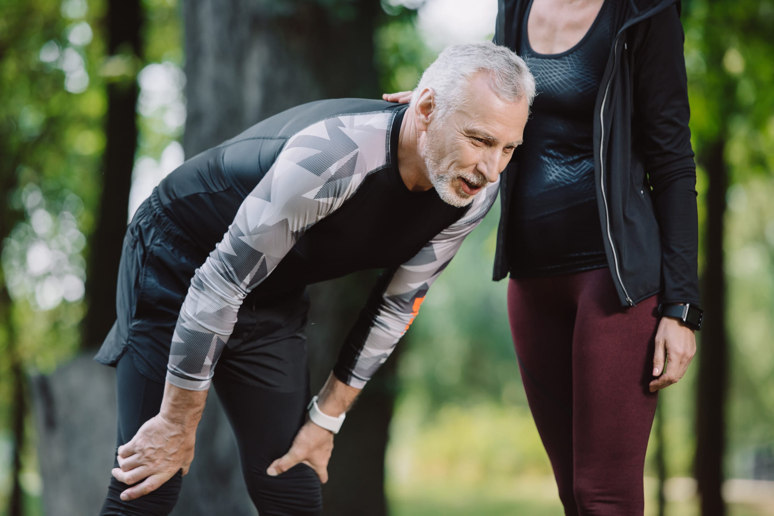 cropped view of sportswoman standing near tired mature sportsman in park