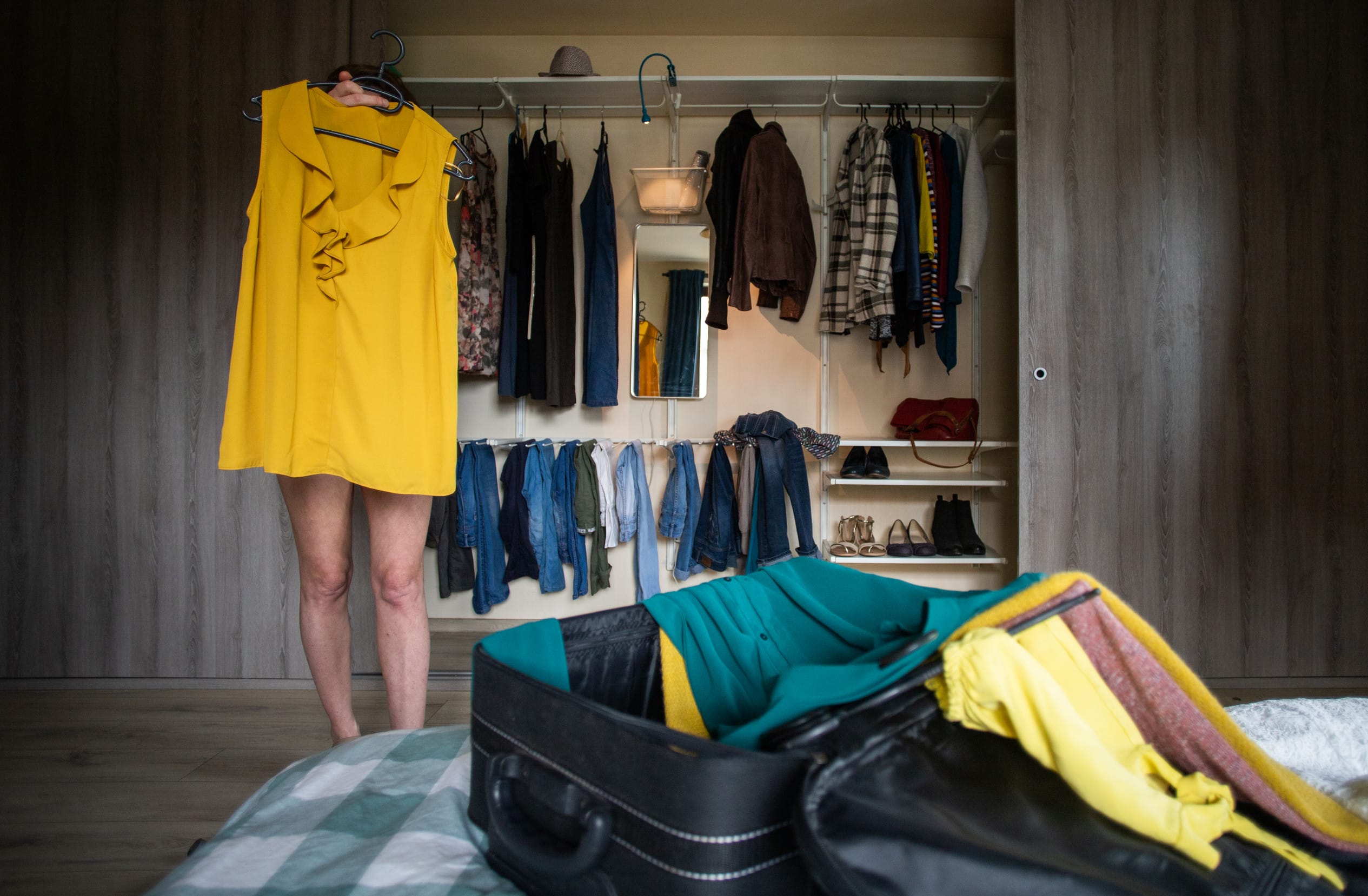 woman packing a suitcase trying on clothes wardrobe in background